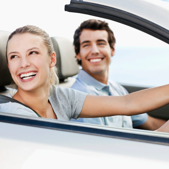 Young man and woman smile back over their shoulders while seated in a convertible car.  Horizontal shot.